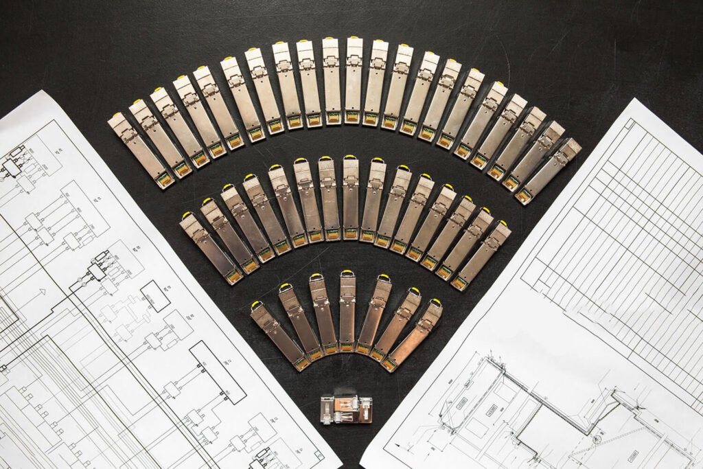 Top view of multiple SFP transceiver modules arranged in a semi-circle with technical engineering blueprints, symbolizing fiber optic network design and data center planning.